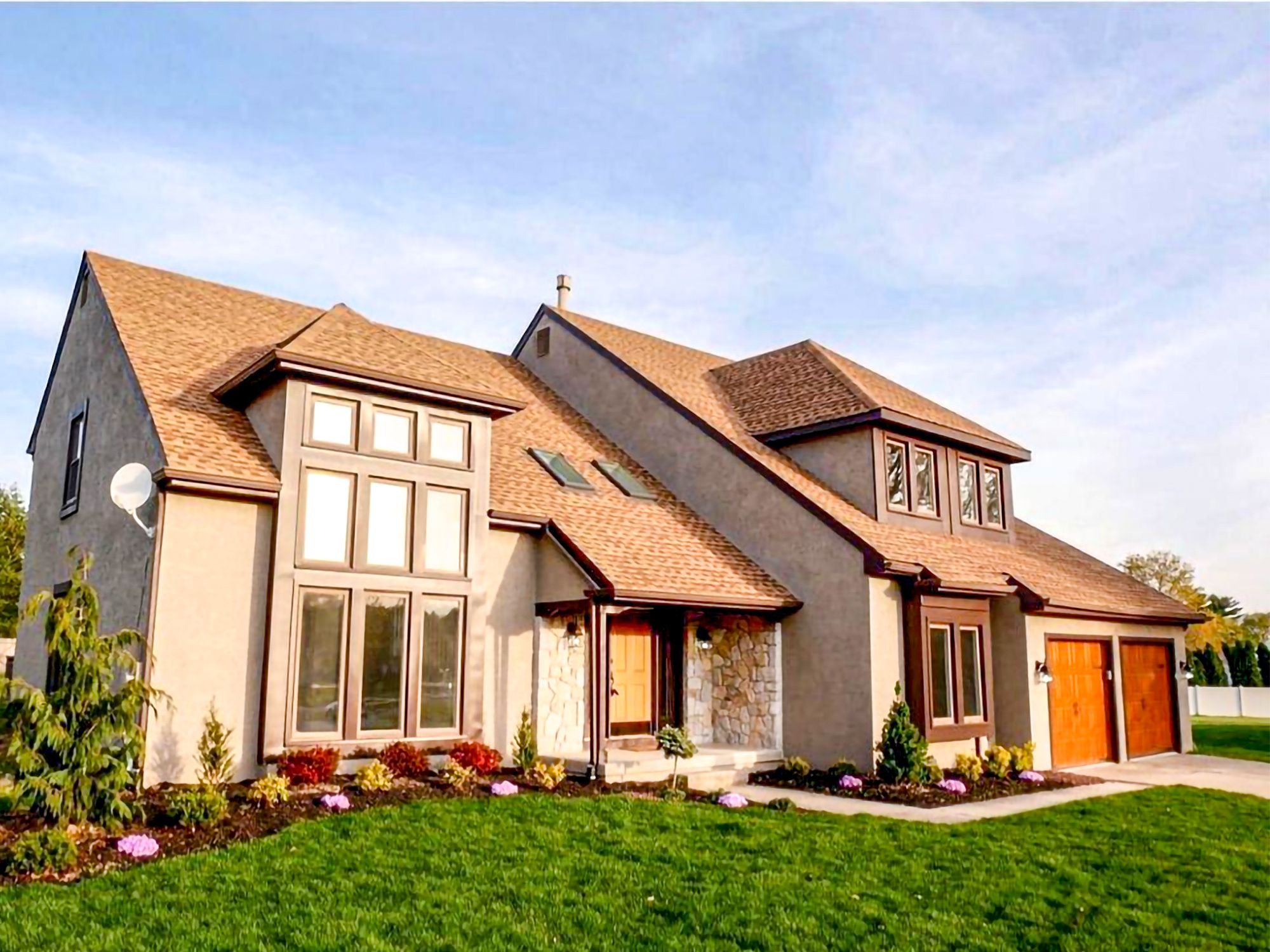 A modern home featuring large rectangular windows, nice landscaping, and skylights on the roof.