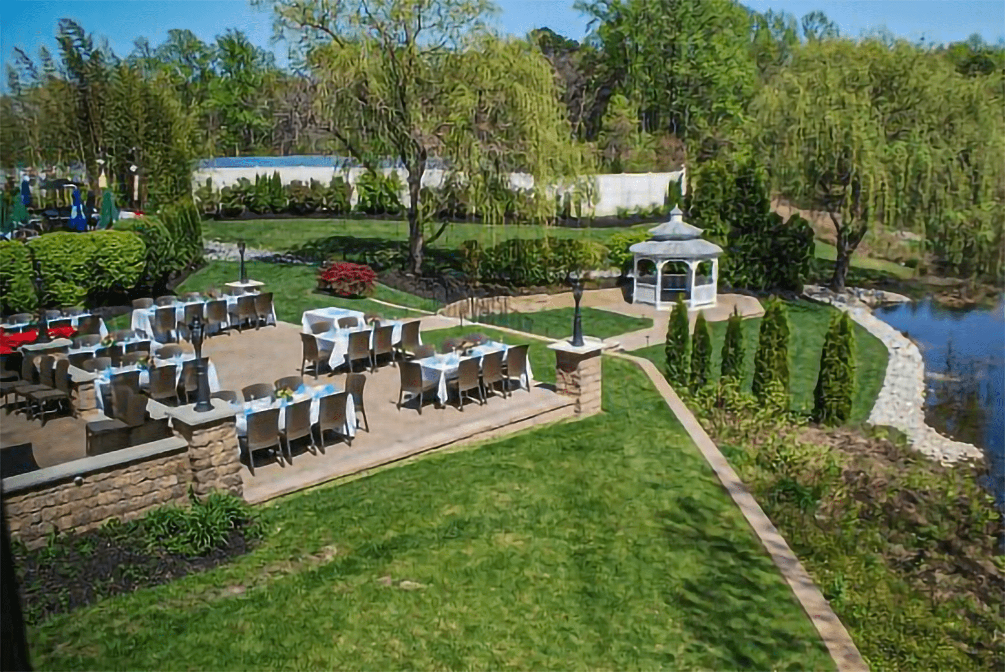 An outdoor space overlooking landscaped grounds and a pond are decorated with tables and chairs for a formal event.