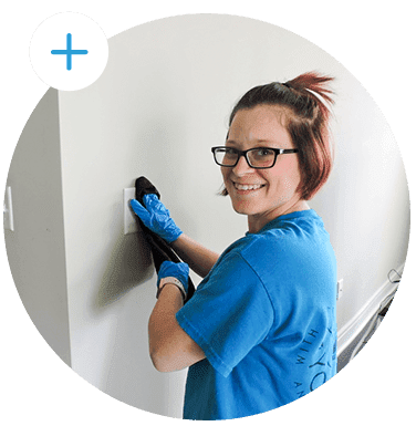 A professional house cleaner from Freshen Your Nest uses a microfiber cloth to clean a light switch and smiles at the camera.
