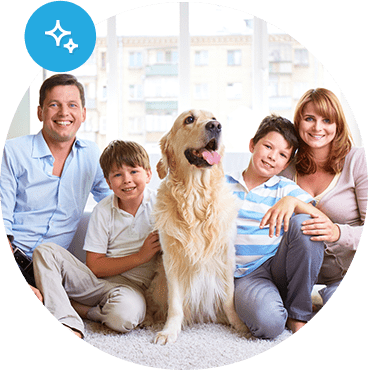 A father, mother, and two young sons smile for a picture with their family dog.