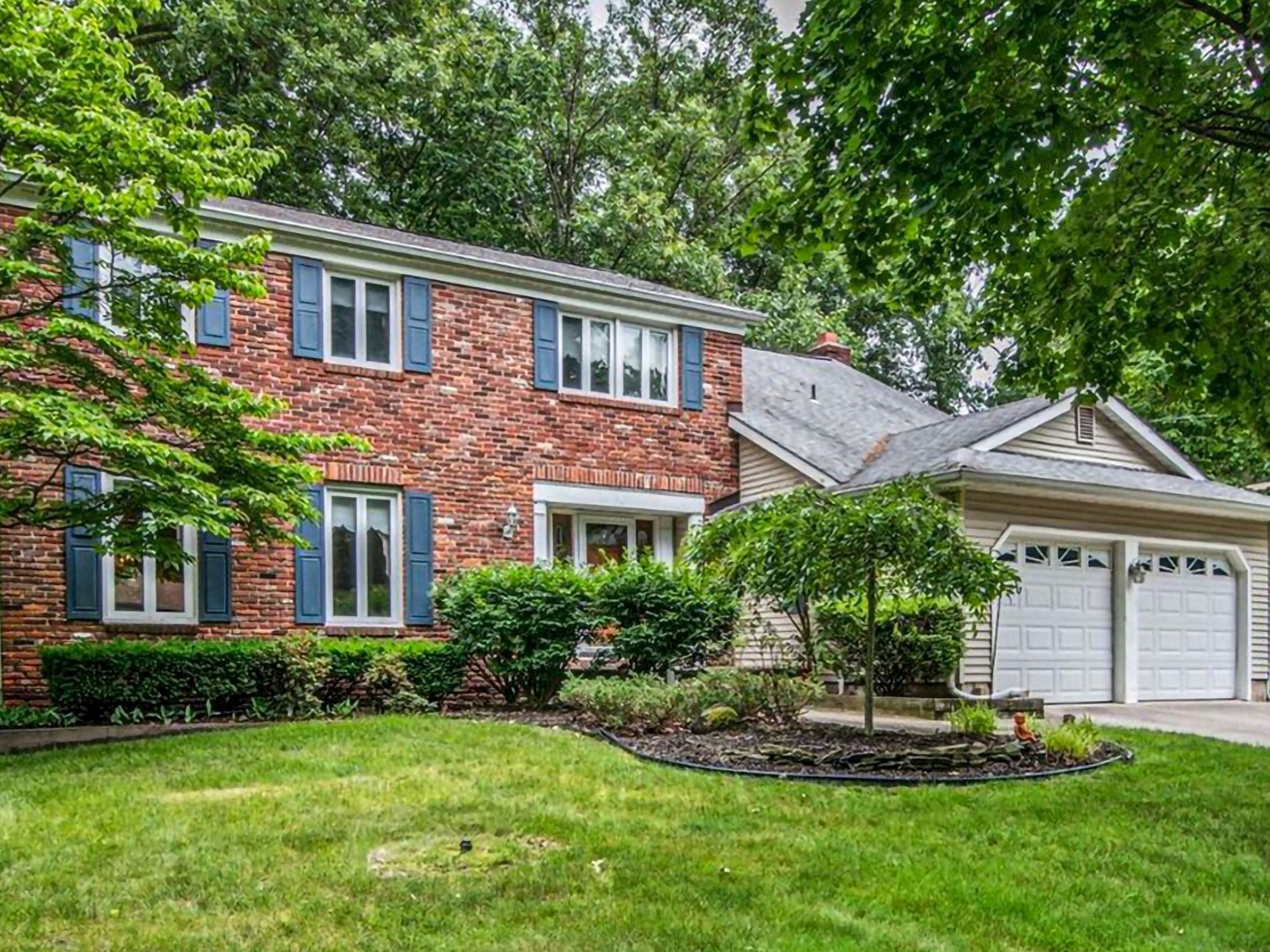 Beautifully landscaped traditional red-brick suburban home with blue shutters and a two-car garage.