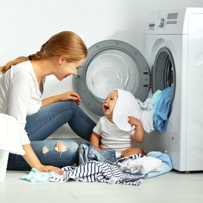 Mother and infant sitting by washing machine surrounded by clean laundry,