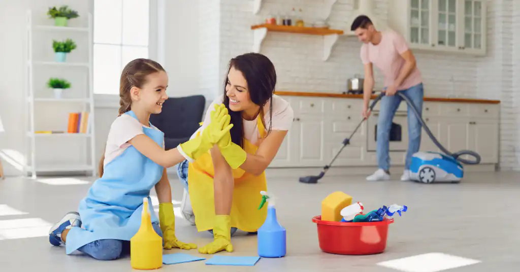 A mother and young daughter high-fiving after cleaning the floor in their kitchen.